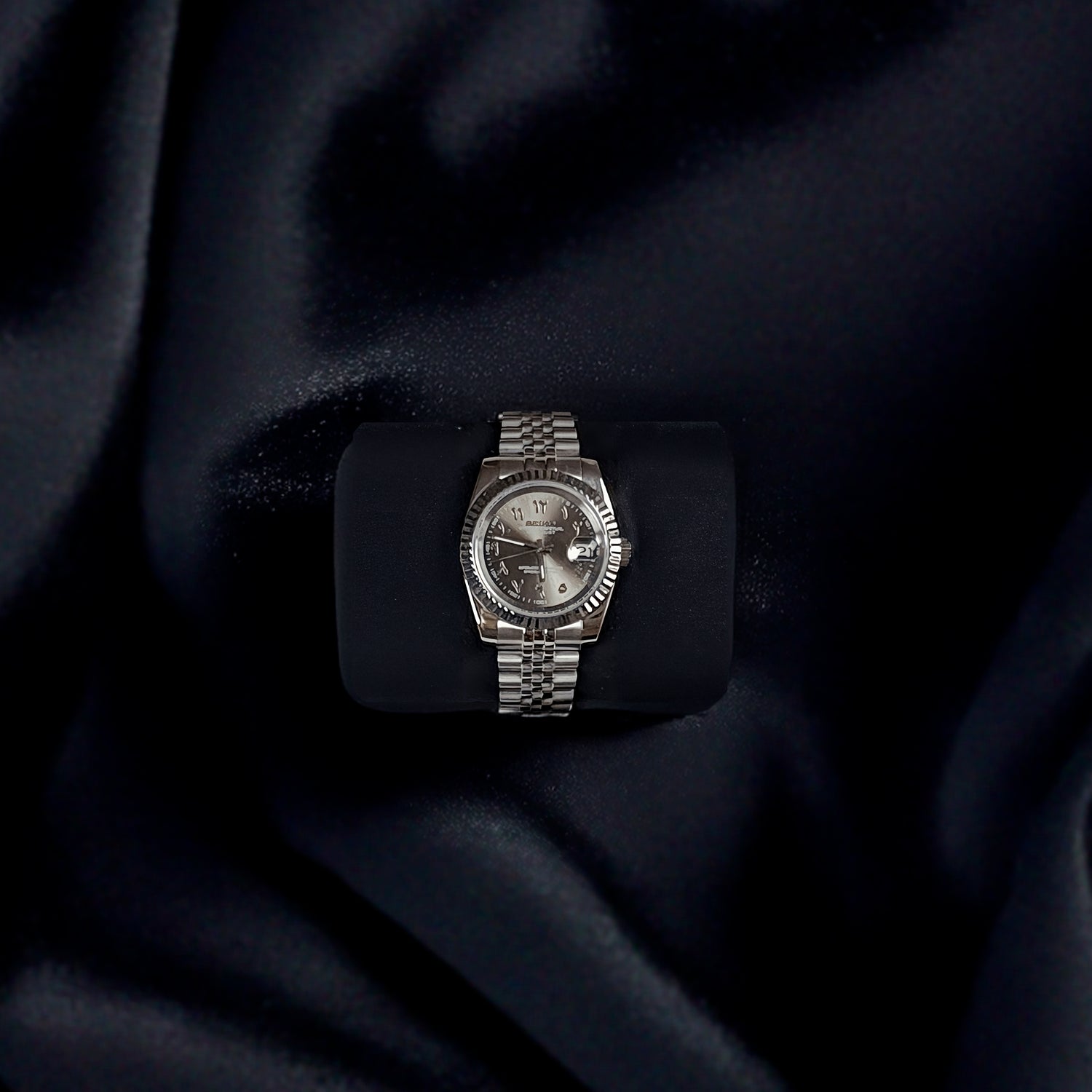 Zoom ind på sølvgrå arabisk Datejust mod ur på sort baggrund.